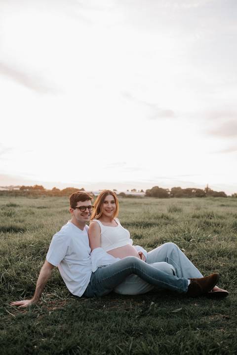 Foto do casal sentado no gramado sorrindo para a câmera.'