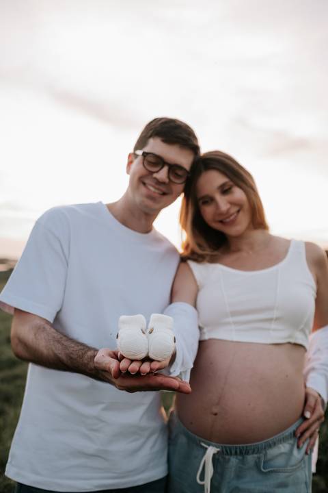 Foto do casal segurando sapatinhos brancos de bebê.'