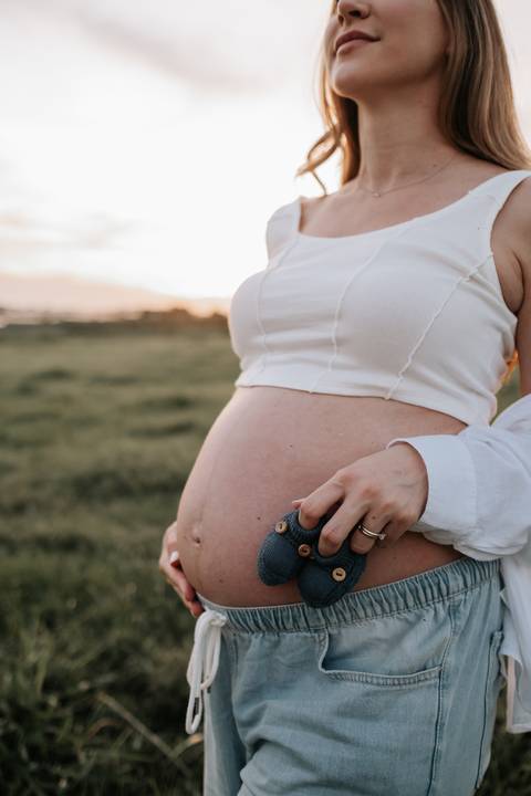 Foto em detalhe da barriga da gestante com sapatinhos azuis.'