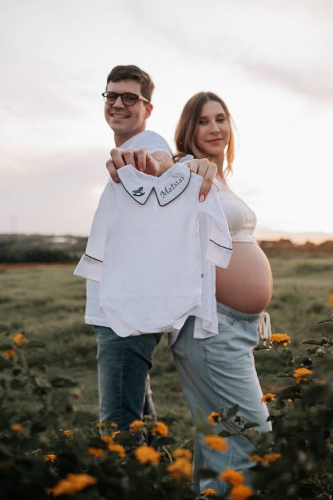 Foto da gestante exibindo um body branco bordado com o nome Mathias.'