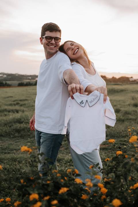 Foto do casal caminhando e segurando o body bordado.'