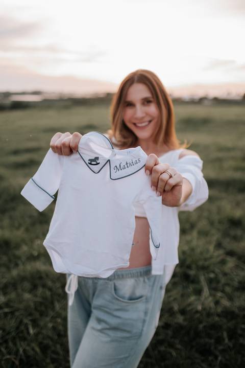 Foto da gestante orgulhosa segurando o body branco do bebê.'