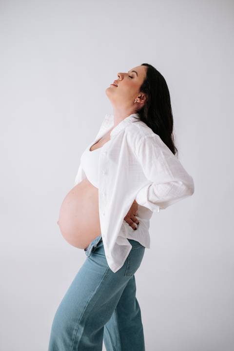 Foto de perfil da gestante com camisa branca aberta em fundo neutro.'