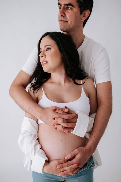 Foto em detalhe das mãos do pai abraçando a barriga por trás.'