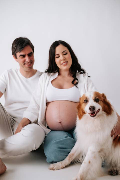 Foto do casal e o pet sorrindo para a câmera em plano aberto.'