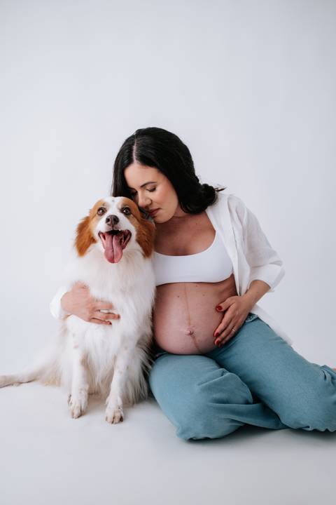 Foto da gestante abraçada ao seu cão destacando a barriga.'