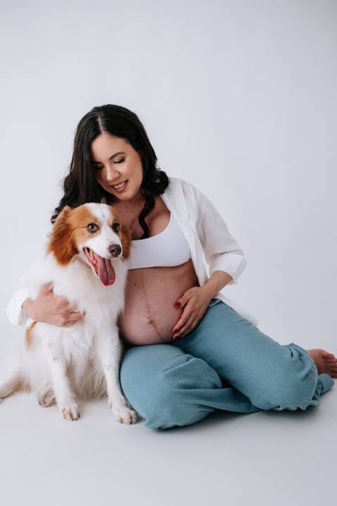 Foto da gestante e o cão sentados em momento descontraído.'