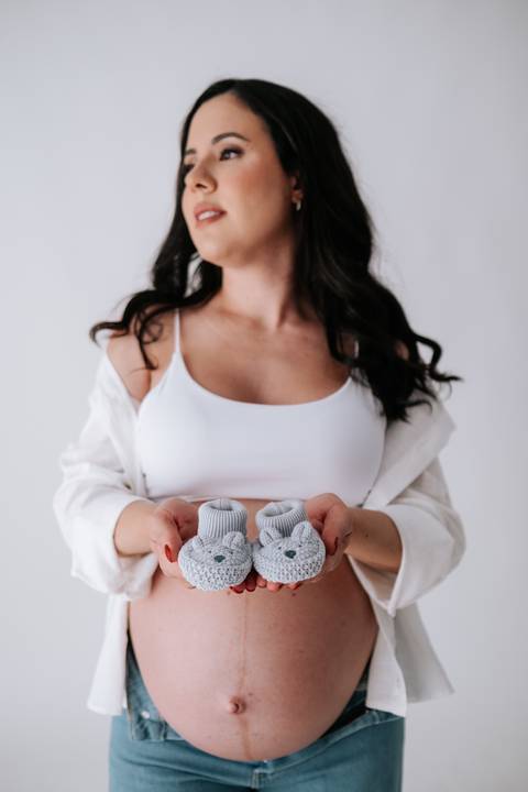 Foto da gestante segurando sapatinhos de bebê cinzas.'