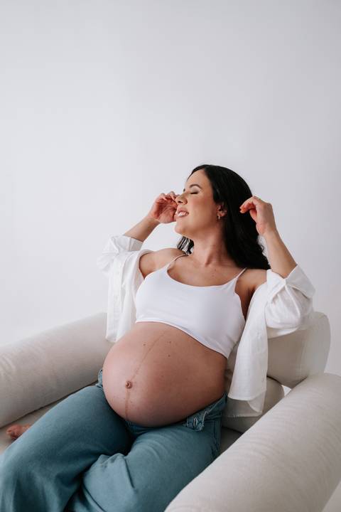 Foto da gestante na poltrona com as mãos no cabelo e olhos fechados.'