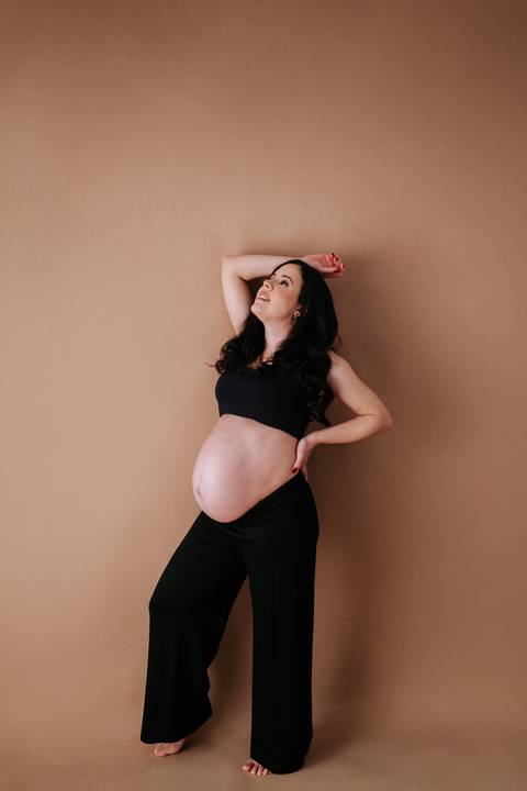 Foto da gestante de perfil com look preto em fundo terracota.'