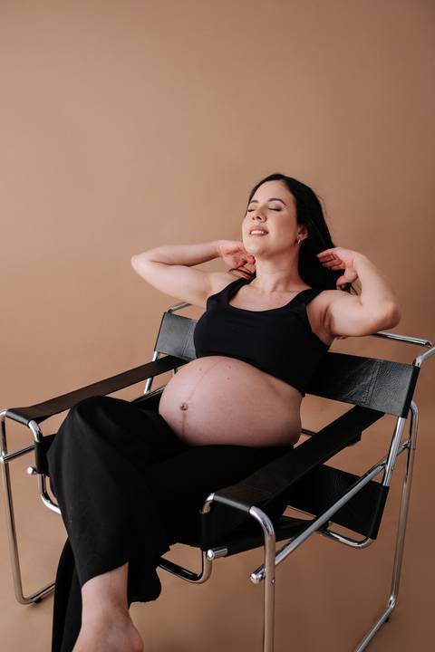 Foto da gestante sentada em uma cadeira de design moderno em estilo editorial.'