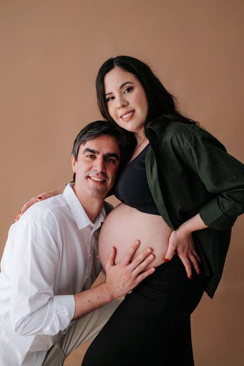 Foto do casal sorrindo com destaque para o rosto e a barriga.'