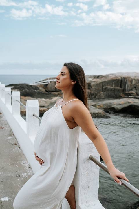 Foto de perfil da gestante com mar e rochas ao fundo.'