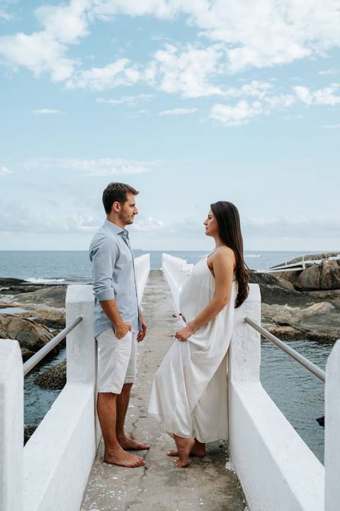 Foto do casal trocando olhares em frente à passarela de madeira.'