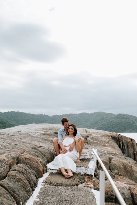 Foto em plano aberto do casal sentado no topo das rochas.'