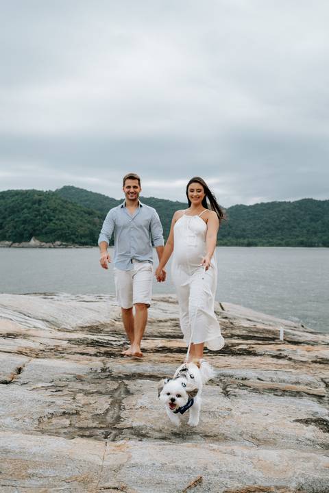 Foto do casal caminhando de mãos dadas em cenário litorâneo.'