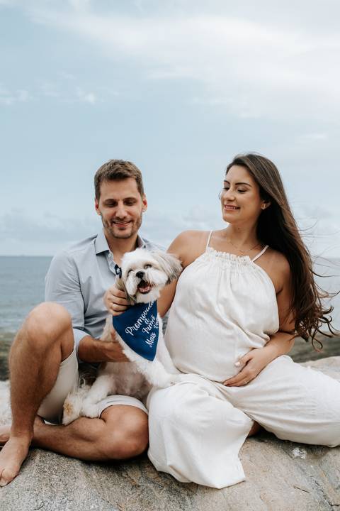 Foto do casal sentado com seu cão de estimação de bandana azul.'