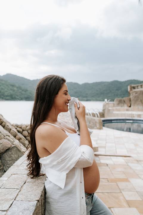 Foto da gestante cheirando uma roupinha de bebê em momento afetivo.'