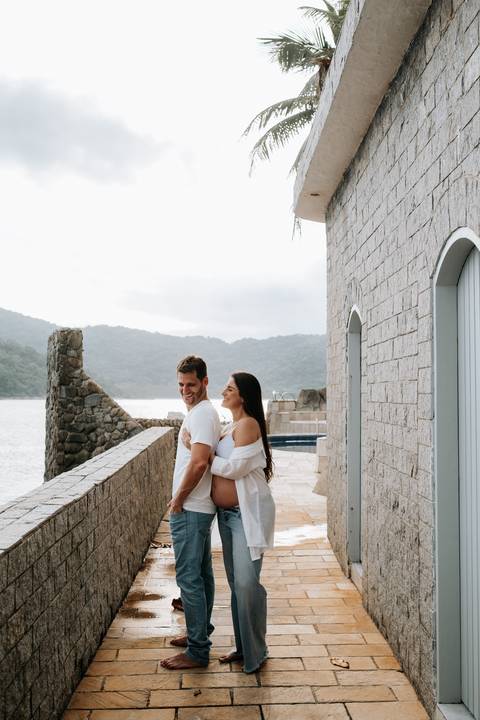 Foto do casal abraçado em um corredor de pedra rústica.'