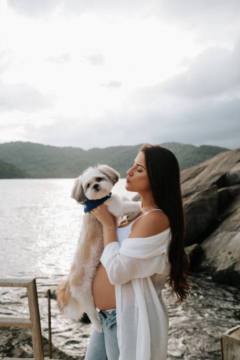 Foto da gestante abraçada ao seu cão de estimação no mar.'