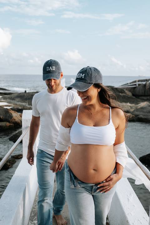Foto do casal caminhando na passarela branca sobre as rochas.'