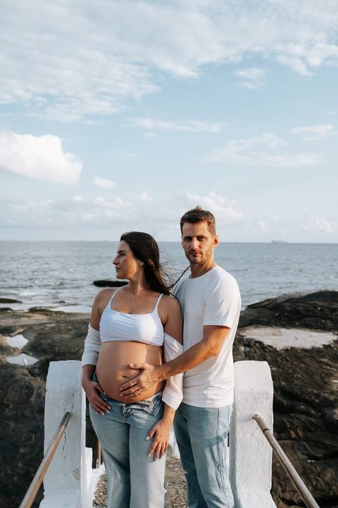 Foto do casal abraçado observando o horizonte da praia.'