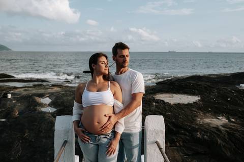 Foto da gestante em destaque com o parceiro a abraçando por trás.'