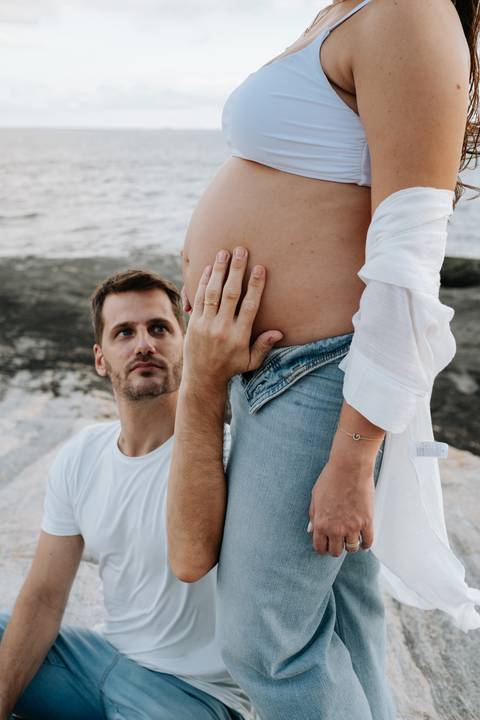 Foto do pai olhando com admiração para a barriga da gestante.'