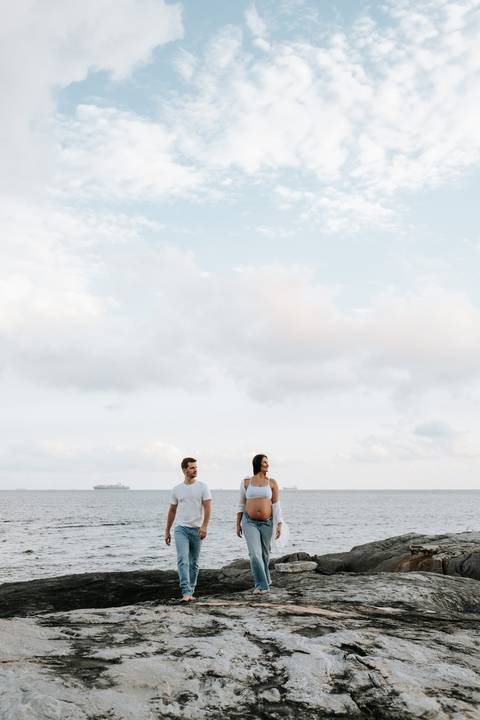 Foto em plano aberto do casal na beira-mar sob um céu claro.'
