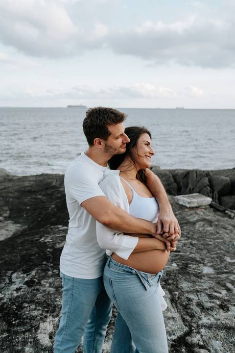 Foto do casal sorridente em momento de carinho nas rochas.'