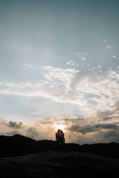 Foto da paisagem do mar com o sol começando a se pôr entre nuvens.'