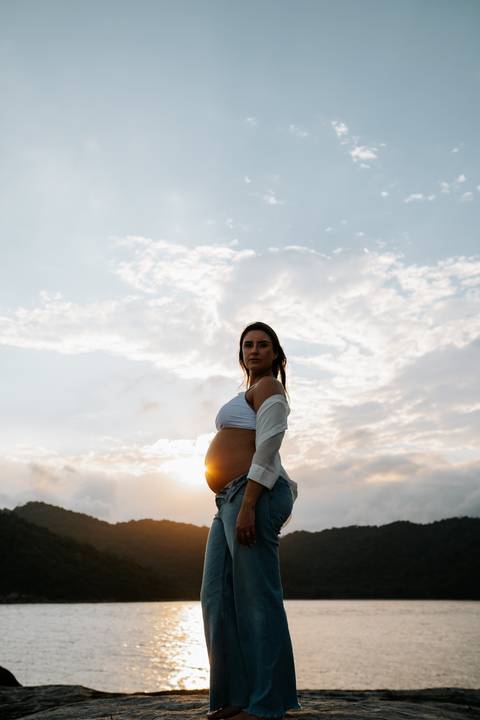 Foto da silhueta da gestante destacando a barriga sob a luz dourada.'