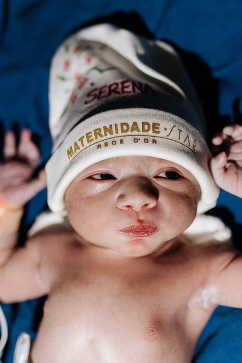 Foto de close do rosto da recém-nascida com touca da maternidade.'