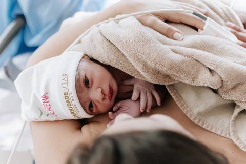 Foto da bebê logo após o nascimento no colo da mãe.'