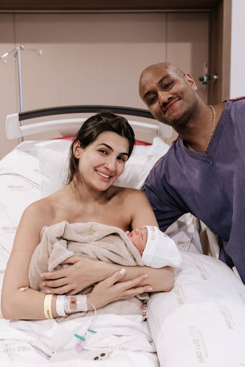 Foto da mãe sorridente segurando a Serena no colo na cama hospitalar.'