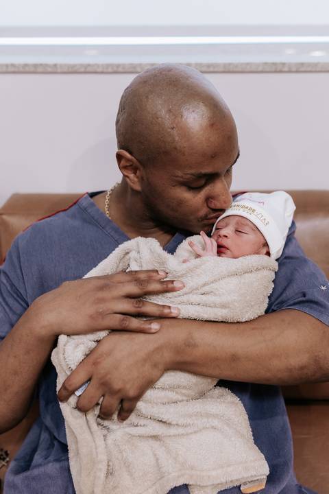 Foto do pai segurando a filha recém-nascida com carinho.'