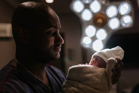 Foto do pai observando a bebê sob a luz da sala de parto.'