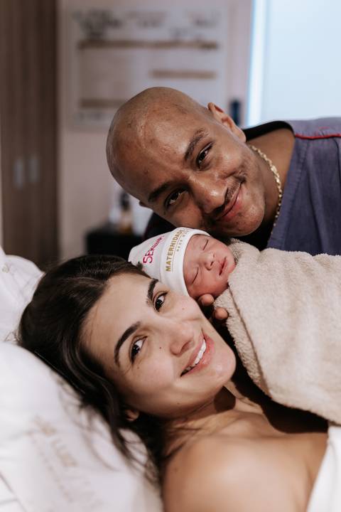 Foto do casal admirando a pequena no pós-parto.'
