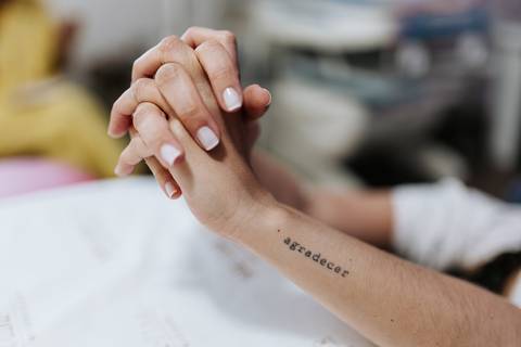 Foto em detalhe das mãos dadas e tatuagem escrita 