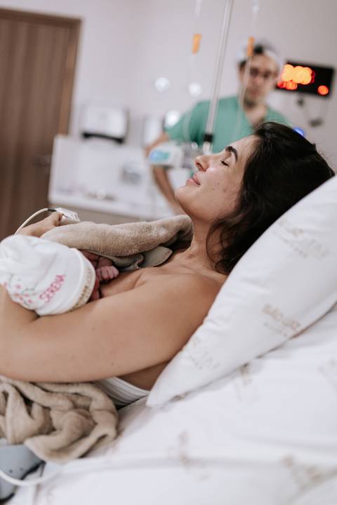 Foto da mãe amamentando pela primeira vez na sala de parto.'