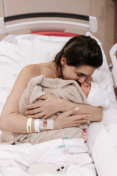 Foto da mãe beijando o rosto da bebê em momento de acolhimento.'