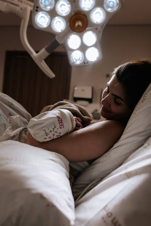 Foto da mãe observando a bebê dormindo no seu colo.'