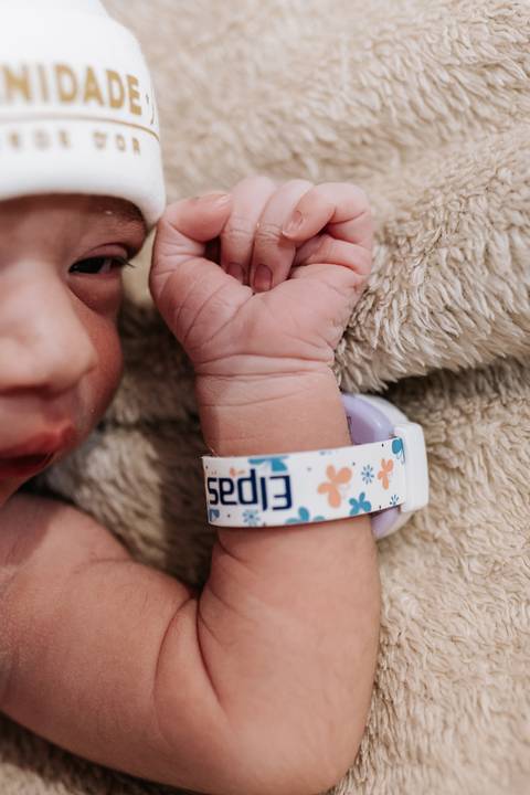 Foto em detalhe do punho da bebê com a pulseira de identificação hospitalar.'