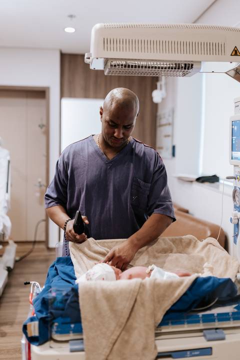 Foto do pai preparando a manta para envolver a bebê.'