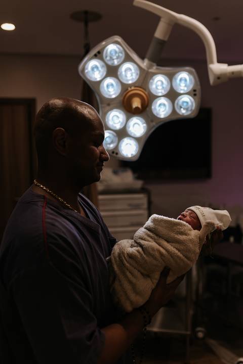 Foto do pai segurando a bebê sob a luz da sala de parto.'