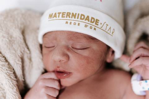 Foto de close da bebê dormindo com touca da maternidade.'