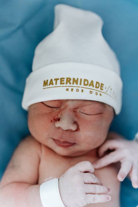 Foto de close do rosto da bebê com touca da maternidade.'