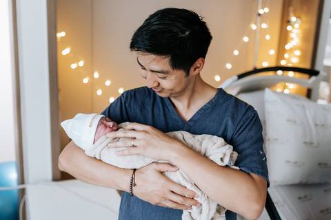 Foto do pai segurando a bebê recém-nascida no colo com carinho.'