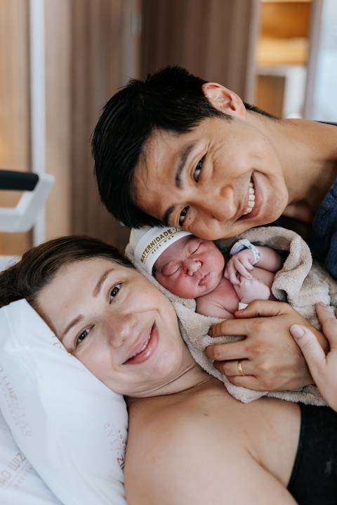 Foto aproximada do rosto do casal e da bebê em plano médio.'