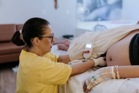 Foto da profissional de saúde realizando ausculta fetal na gestante.'